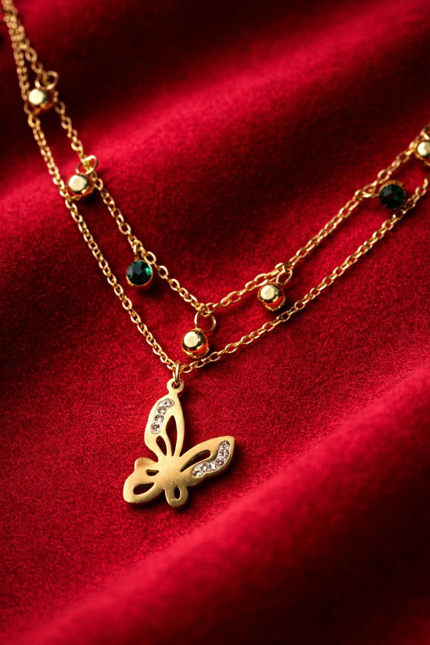 Gold-tone butterfly charm necklace with bead accents on red fabric background
