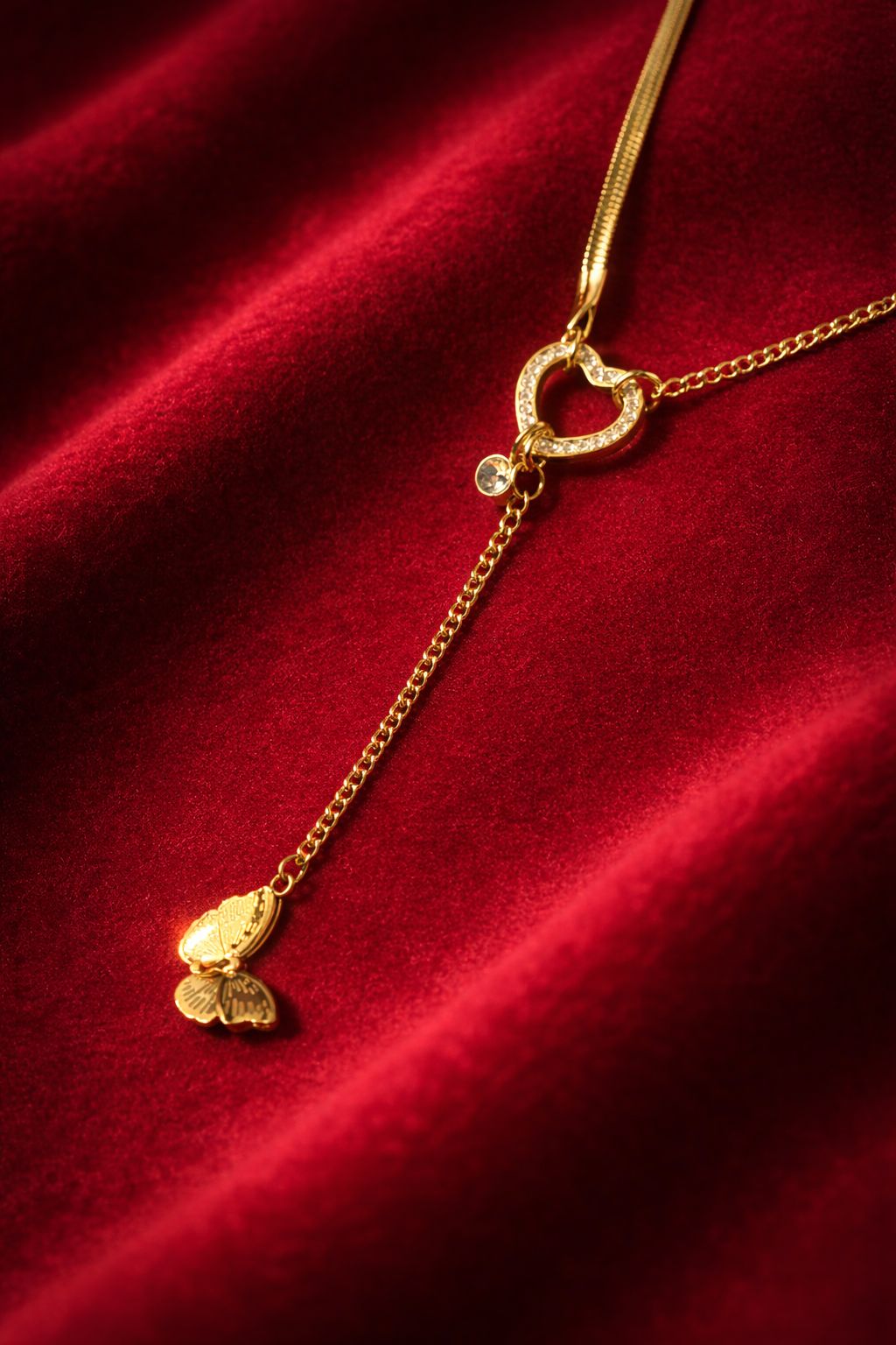 Gold-tone necklace with heart loop and butterfly drop pendant on red fabric