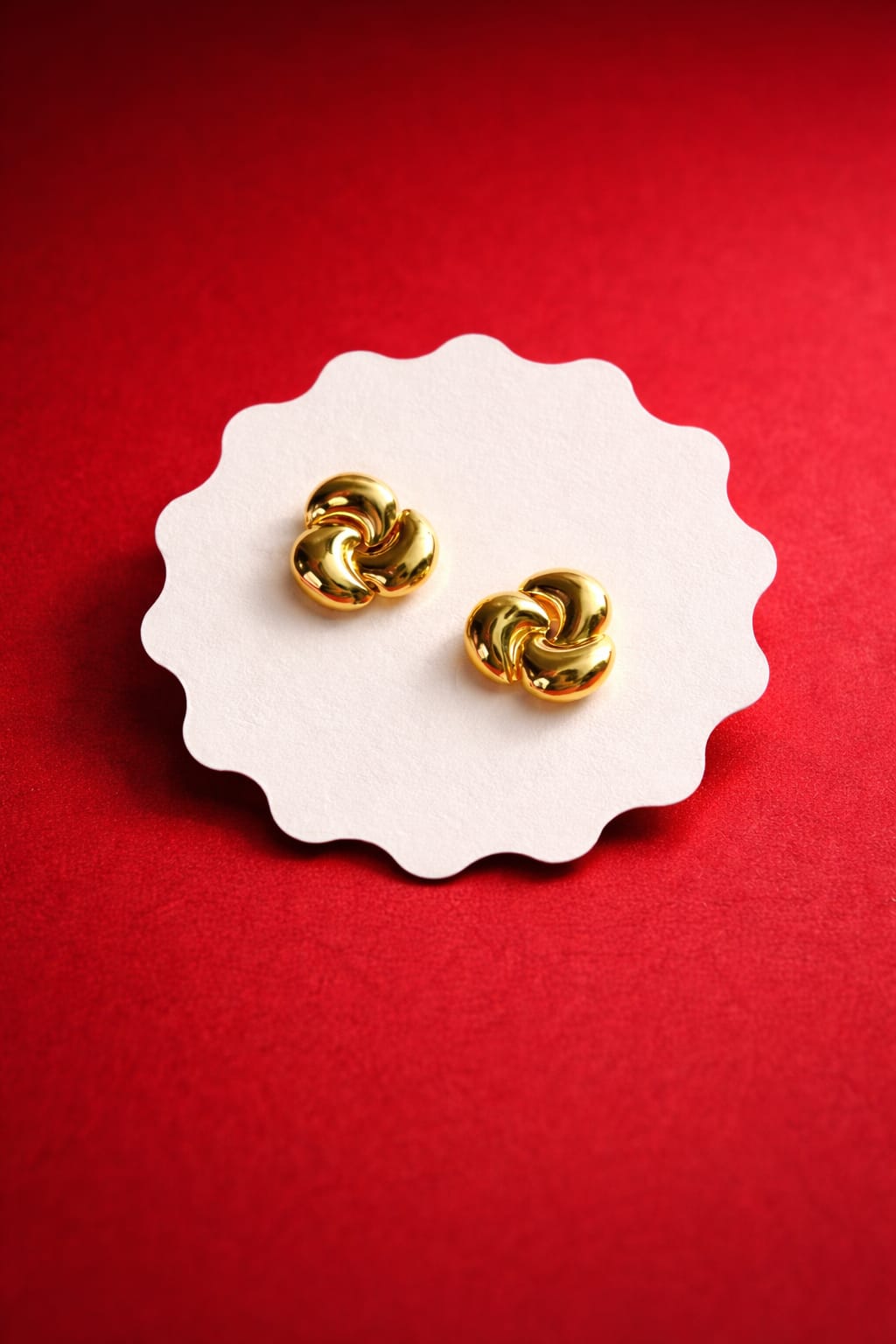 Gold-tone swirl knot stud earrings displayed on white card with red background