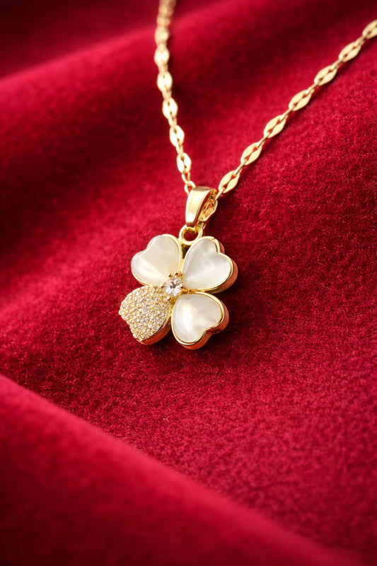 Gold-tone clover pendant necklace with pearl-look petals on red velvet background

