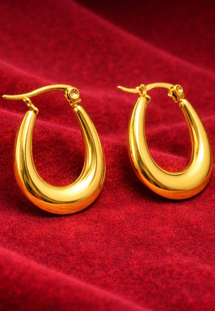Gold-tone curved hoop earrings with glossy finish on red velvet background
