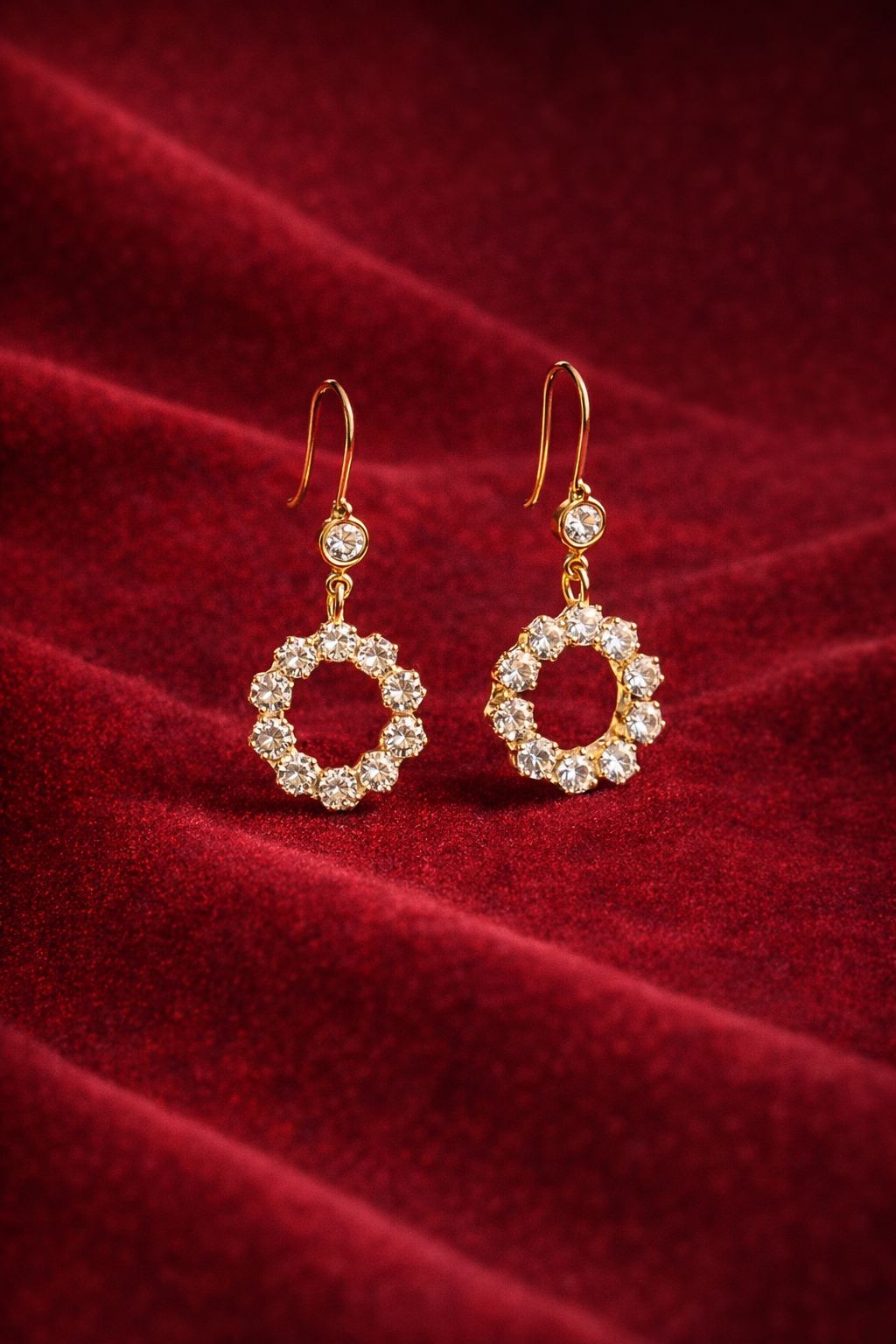 Gold-tone crystal halo drop earrings held in hand with outdoor background