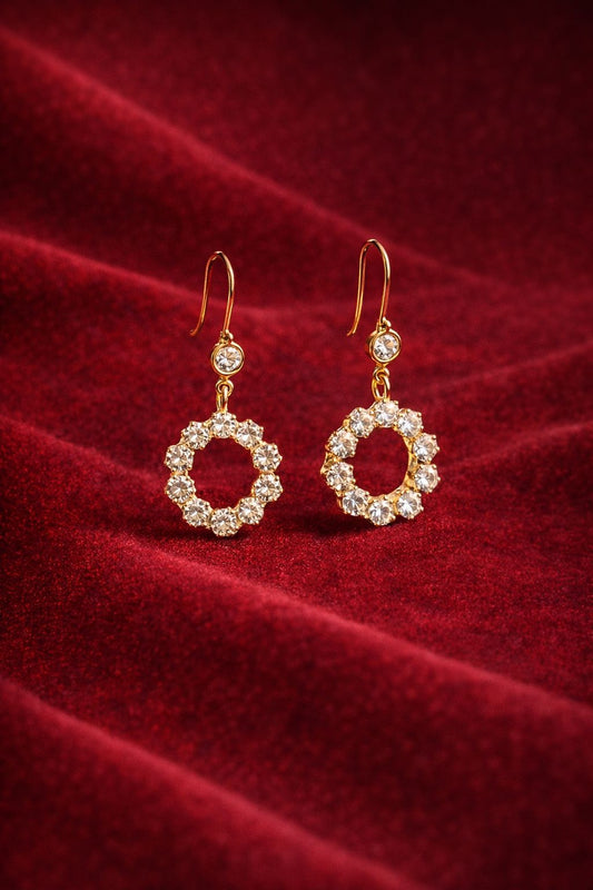 Gold-tone crystal halo drop earrings held in hand with outdoor background