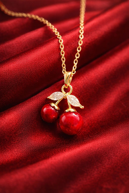Gold plated cherry pendant necklace with crystal leaves on red velvet background