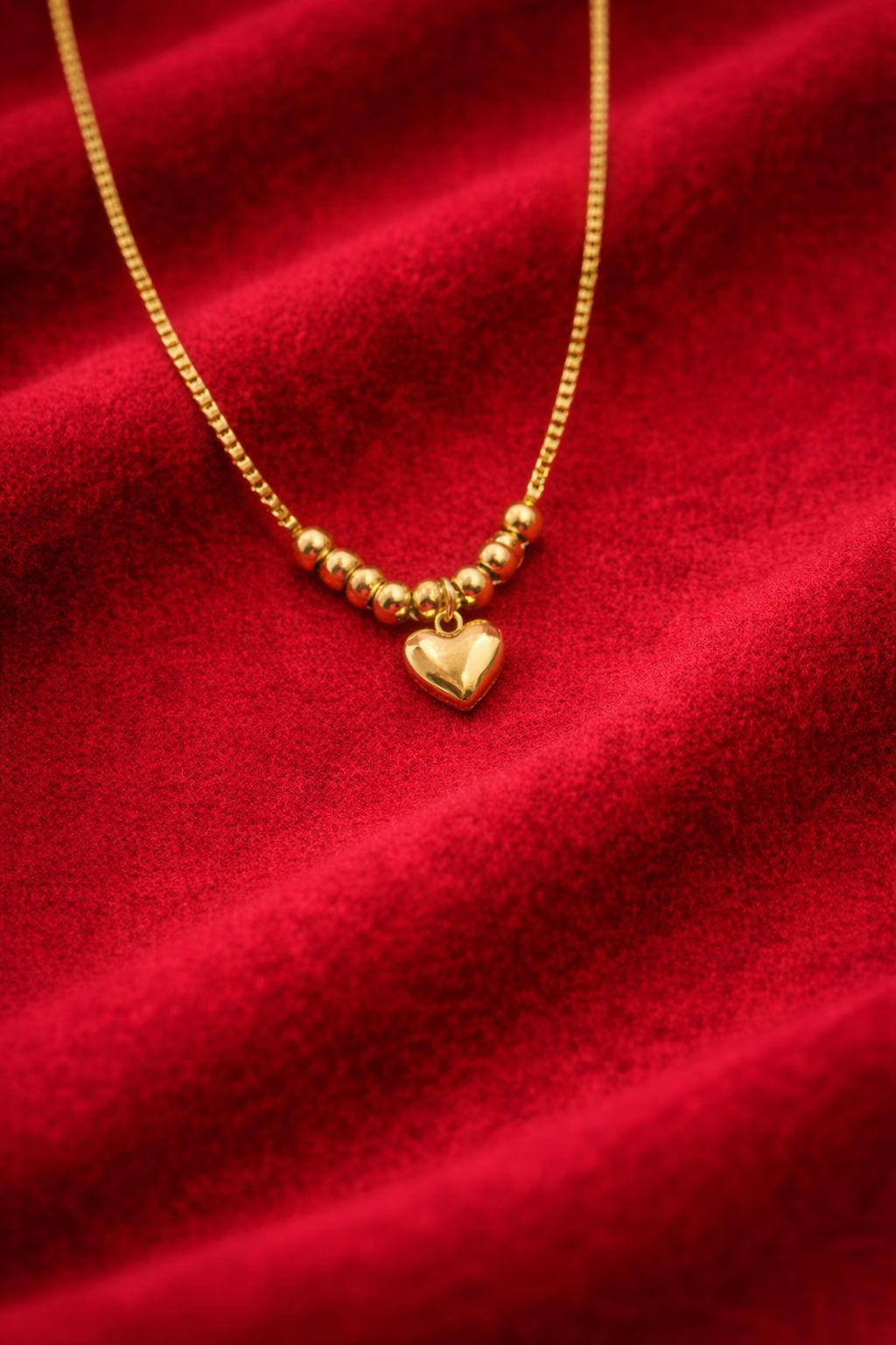 Gold necklace with a heart pendant on a red fabric background