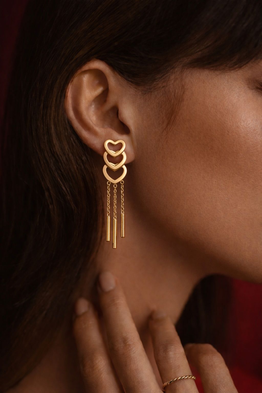 Gold plated triple heart chain drop earrings worn by woman and displayed on red velvet background