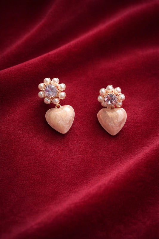 Pair of earrings with heart and floral design on a red fabric background
