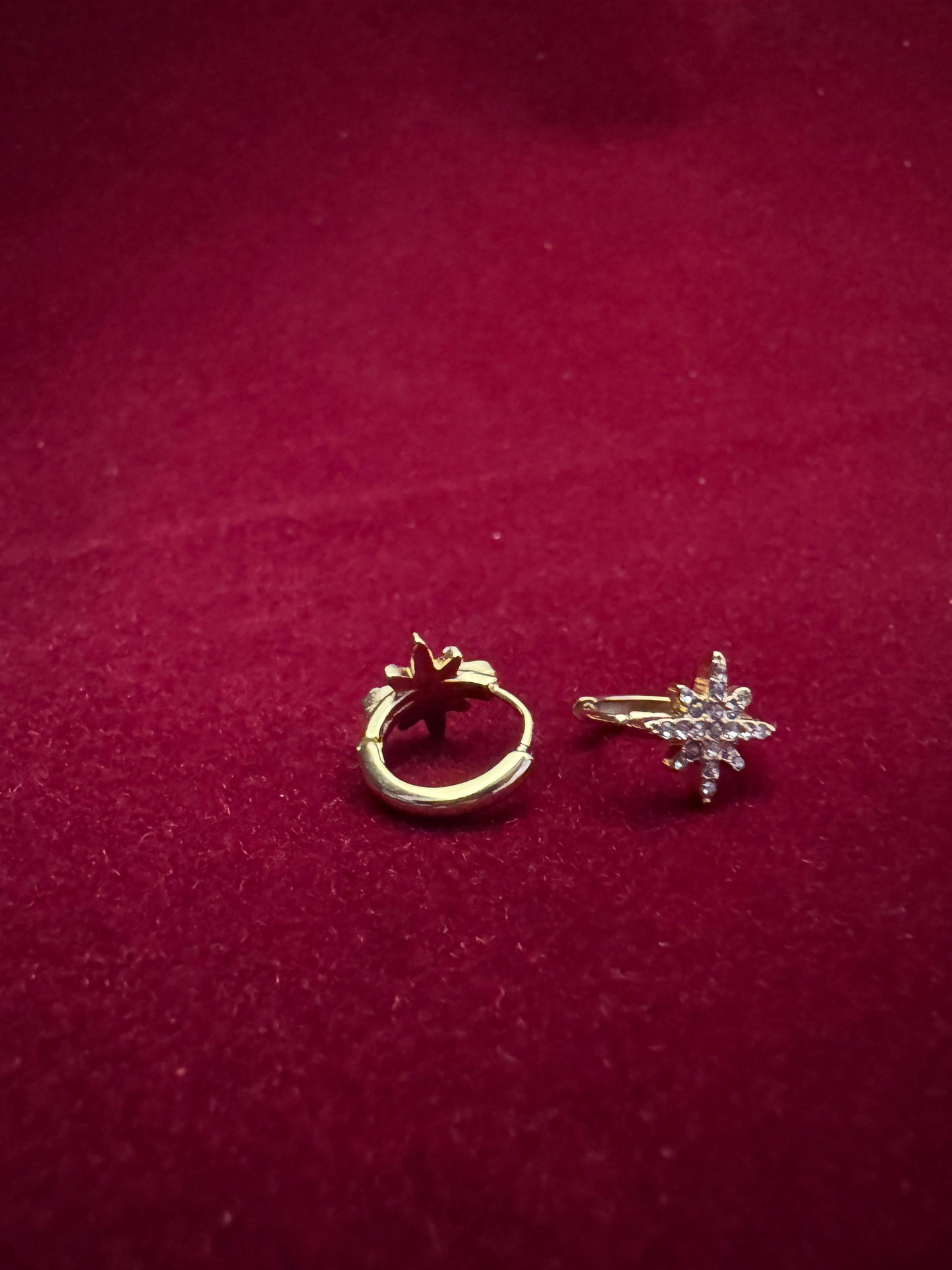 Gold hoop earring and star-shaped earring on a red background