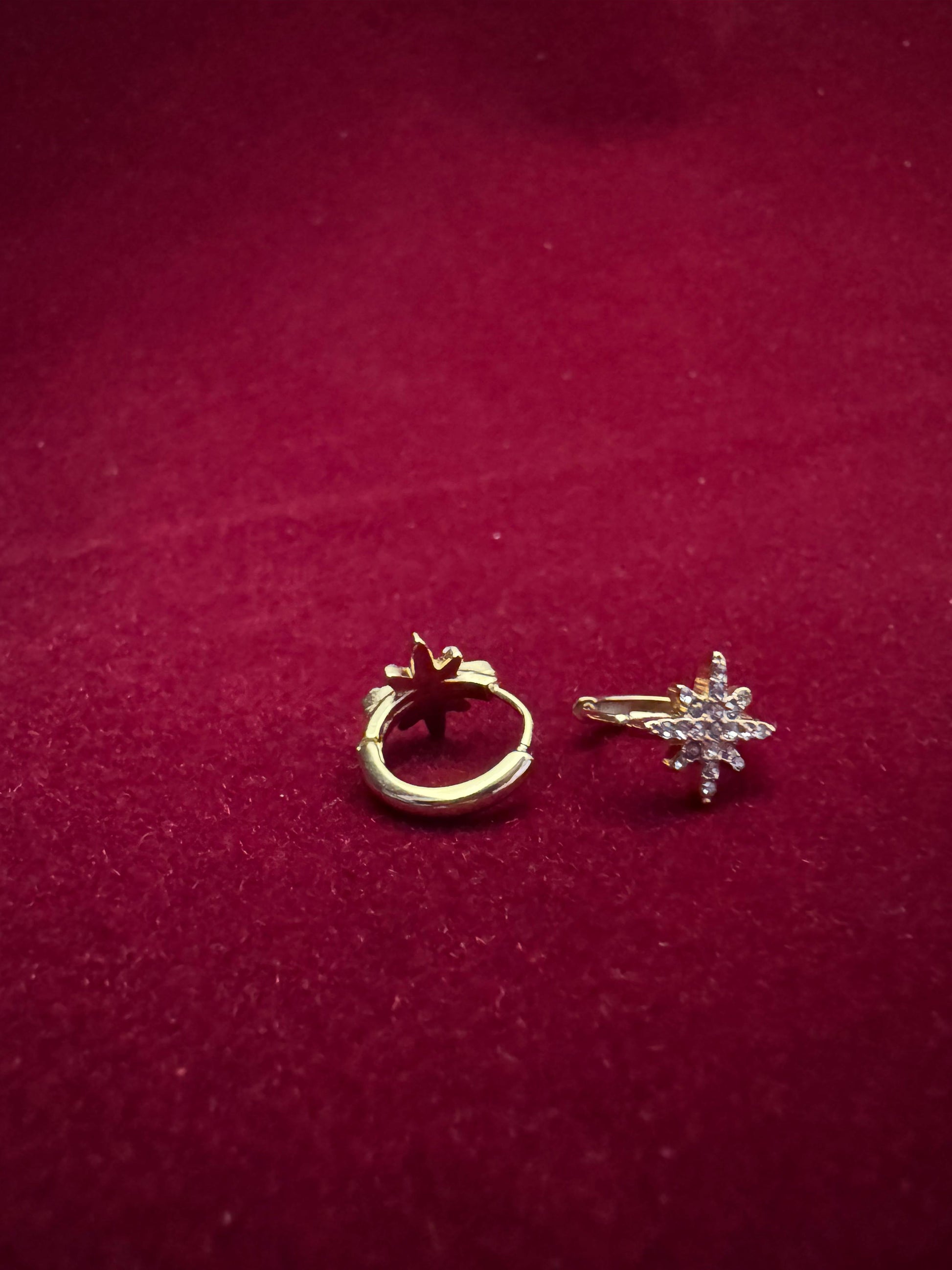 Gold hoop earring and star-shaped earring on a red background